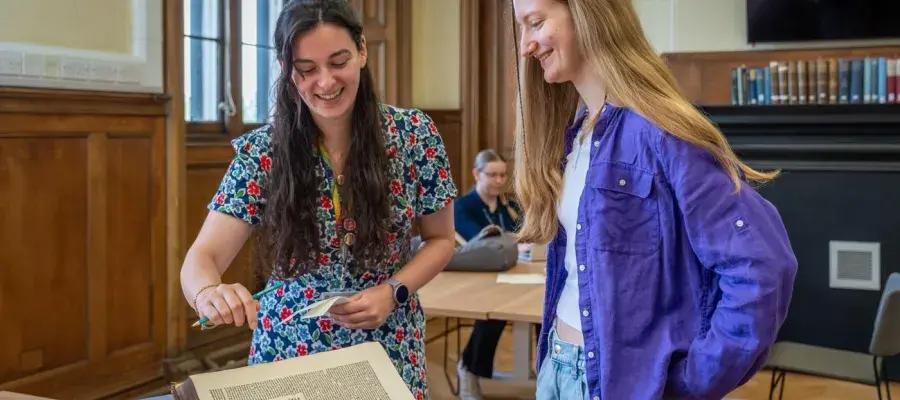 A member of staff showing a student a book in the New College Funk Reading Rom